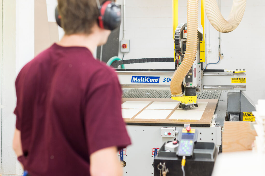 Mitarbeiter beobachtet wie die CNC-Maschine die Holzplatten fräst